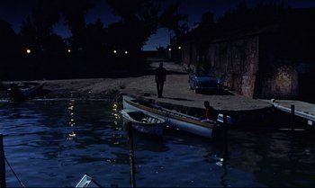 Movie still from “Dr. No” (1962), directed by Terence Young – A man standing next to a boat on a body of water at night; Extreme Wide shot, High angle
