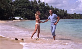 Movie still from “Dr. No” (1962), directed by Terence Young – A man and a woman holding hands on the beach; Wide shot, High angle