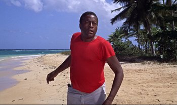 Movie still from “Dr. No” (1962), directed by Terence Young – A man standing on the beach wearing a red shirt; Medium shot, Low angle