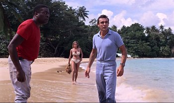 Movie still from “Dr. No” (1962), directed by Terence Young – A man and a woman walking on the beach with another man; Wide shot, Over the shoulder angle