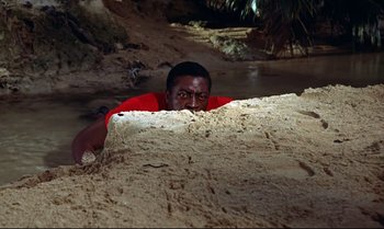 Movie still from “Dr. No” (1962), directed by Terence Young – A man in a red shirt laying on the ground; Medium shot, High angle