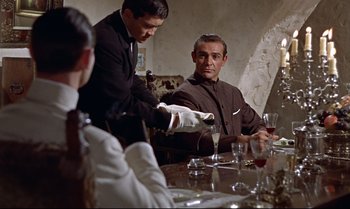 Movie still from “Dr. No” (1962), directed by Terence Young – A man pouring a glass of wine at a dinner table; Medium shot, Over the shoulder angle
