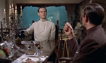 Movie still from “Dr. No” (1962), directed by Terence Young – A man sitting at a dinner table in front of another man; Medium shot, Over the shoulder angle