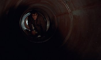 Movie still from “Dr. No” (1962), directed by Terence Young – A man is inside a large metal pipe; Wide shot, Overhead angle