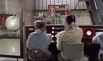 Movie still from “Dr. No” (1962), directed by Terence Young – Two men wearing helmets and sitting in front of a control panel; Wide shot, High angle