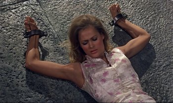 Movie still from “Dr. No” (1962), directed by Terence Young – A woman in a pink dress lying on the ground with her hands tied; Medium shot, High angle