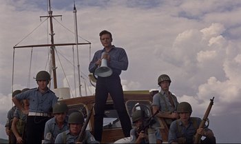 Movie still from “Dr. No” (1962), directed by Terence Young – A man standing on top of a boat next to a group of soldiers; Medium shot, Low angle