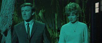 Movie still from “Dr. Who and the Daleks” (1965), directed by Gordon Flemyng – A man and a woman standing next to each other in front of trees; Medium shot, Low angle