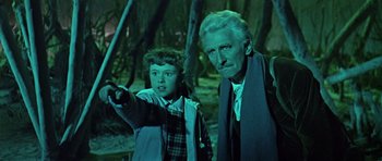 Movie still from “Dr. Who and the Daleks” (1965), directed by Gordon Flemyng – An older man and a young boy are standing in the woods; Medium shot, High angle