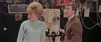 Movie still from “Dr. Who and the Daleks” (1965), directed by Gordon Flemyng – A man and a woman standing next to each other in a room; Medium shot, Low angle