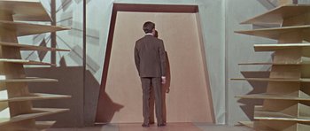 Movie still from “Dr. Who and the Daleks” (1965), directed by Gordon Flemyng – A man in a suit standing in front of an open door; Wide shot, High angle