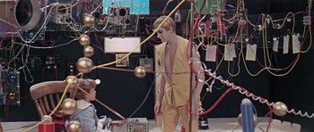 Movie still from “Dr. Who and the Daleks” (1965), directed by Gordon Flemyng – A man standing next to another man in a room with many wires; Medium shot, High angle