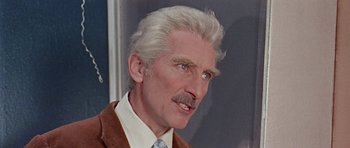 Movie still from “Dr. Who and the Daleks” (1965), directed by Gordon Flemyng – An older man with white hair wearing a suit and tie; Close Up shot, Over the shoulder angle