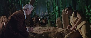 Movie still from “Dr. Who and the Daleks” (1965), directed by Gordon Flemyng – An older man is looking at a piece of wood; Medium shot, High angle