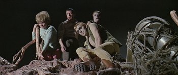 Movie still from “Dr. Who and the Daleks” (1965), directed by Gordon Flemyng – A man crouching on the ground in front of other men; Wide shot, Low angle