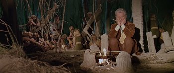 Movie still from “Dr. Who and the Daleks” (1965), directed by Gordon Flemyng – A group of people sitting around a fire pit; Wide shot, High angle