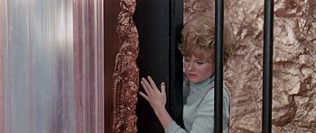 Movie still from “Dr. Who and the Daleks” (1965), directed by Gordon Flemyng – A woman leaning against a wall with her hand on the side of the wall; Medium shot, High angle