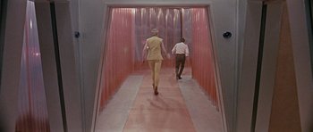 Movie still from “Dr. Who and the Daleks” (1965), directed by Gordon Flemyng – A man and a woman are walking down a hallway; Wide shot, Low angle