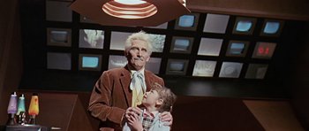Movie still from “Dr. Who and the Daleks” (1965), directed by Gordon Flemyng – An older man and a young boy are standing in front of a television; Medium shot, Low angle