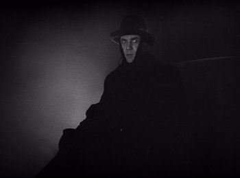 Movie still from “Dracula” (1931), directed by Tod Browning – A man wearing a hat sitting on top of a couch; Medium shot, Low angle