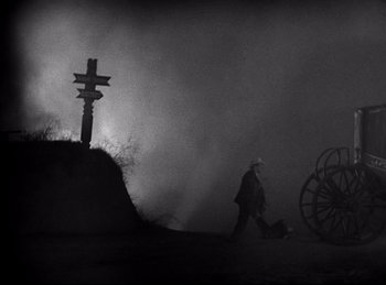 Movie still from “Dracula” (1931), directed by Tod Browning – A man walking in front of a cross on a foggy night; Wide shot, High angle