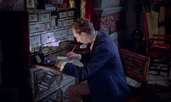 Movie still from “Horror of Dracula” (1958), directed by Terence Fisher – A man sitting at a table writing on a piece of paper; Medium shot, High angle