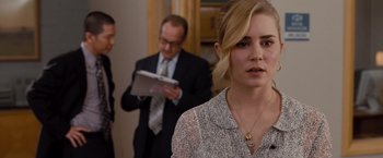 Movie still from “Drag Me to Hell” (2009), directed by Sam Raimi – A woman in a white shirt is looking at the camera while a man in a suit and tie looks on; Close Up shot, Over the shoulder angle