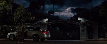 Movie still from “Drag Me to Hell” (2009), directed by Sam Raimi – A car parked on the side of the road under a cloudy night sky; Wide shot, Low angle