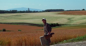 Movie still from “Dreams” (1990), directed by Akira Kurosawa – A man standing in the middle of a field holding a suitcase; Wide shot, Low angle