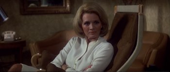 Movie still from “Dressed to Kill” (1980), directed by Brian De Palma – A woman sitting in a chair with her arms crossed; Close Up shot, Over the shoulder angle