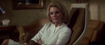 Movie still from “Dressed to Kill” (1980), directed by Brian De Palma – An older woman sitting in a chair with her arms crossed; Close Up shot, Over the shoulder angle