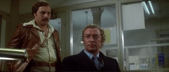 Movie still from “Dressed to Kill” (1980), directed by Brian De Palma – A man in a suit and tie standing next to another man in a suit and tie; Medium shot, Low angle