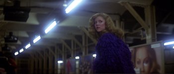 Movie still from “Dressed to Kill” (1980), directed by Brian De Palma – A woman in a purple coat standing in a building; Medium shot, Low angle