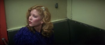 Movie still from “Dressed to Kill” (1980), directed by Brian De Palma – A woman sitting on a bench wearing a blue dress; Close Up shot, Over the shoulder angle
