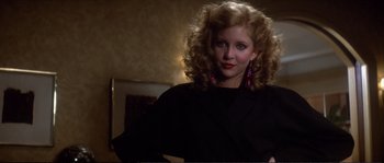 Movie still from “Dressed to Kill” (1980), directed by Brian De Palma – A woman in a black shirt and pink earrings is posing; Close Up shot, Low angle