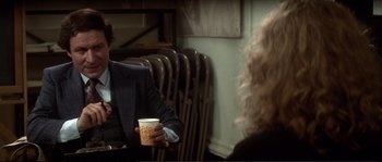 Movie still from “Dressed to Kill” (1980), directed by Brian De Palma – A man in a suit holding a cup of coffee; Medium shot, Over the shoulder angle
