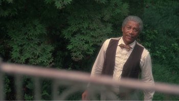 Movie still from “Driving Miss Daisy” (1989), directed by Bruce Beresford – An older man standing in front of some bushes; Medium shot, Over the shoulder angle