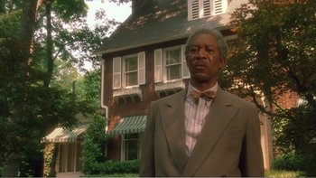 Movie still from “Driving Miss Daisy” (1989), directed by Bruce Beresford – An older man wearing a suit and bow tie in front of a house; Medium shot, Low angle