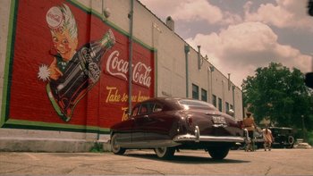 Movie still from “Driving Miss Daisy” (1989), directed by Bruce Beresford – An old car parked in front of a coca - cola advertisement; Extreme Wide shot, Low angle
