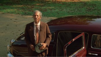 Movie still from “Driving Miss Daisy” (1989), directed by Bruce Beresford – An older man standing next to a parked car; Wide shot, High angle
