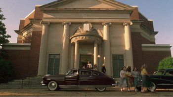 Movie still from “Driving Miss Daisy” (1989), directed by Bruce Beresford – A car parked in front of a building with people standing around; Extreme Wide shot, High angle