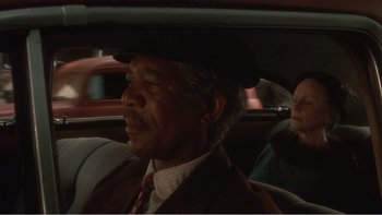 Movie still from “Driving Miss Daisy” (1989), directed by Bruce Beresford – A man in a hat sitting in the back seat of a car; Close Up shot, Over the shoulder angle