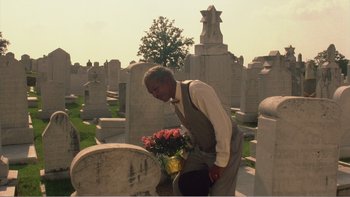 Movie still from “Driving Miss Daisy” (1989), directed by Bruce Beresford – A man in a vest and tie standing in front of a grave; Wide shot, Low angle