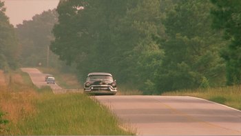 Movie still from “Driving Miss Daisy” (1989), directed by Bruce Beresford – A couple of cars driving down a road next to trees; Extreme Wide shot, High angle