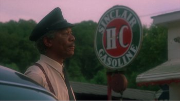 Movie still from “Driving Miss Daisy” (1989), directed by Bruce Beresford – A man standing in front of a gas station sign; Close Up shot, Over the shoulder angle