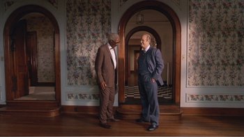 Movie still from “Driving Miss Daisy” (1989), directed by Bruce Beresford – Two men in suits standing next to each other in a room; Wide shot, Over the shoulder angle