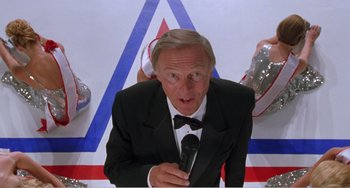 Movie still from “Drop Dead Gorgeous” (1999), directed by Michael Patrick Jann – An older man in a tuxedo holding a microphone; Medium shot, Low angle