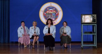 Movie still from “Drop Dead Gorgeous” (1999), directed by Michael Patrick Jann – A group of women sitting on top of chairs in front of a blue background; Wide shot, High angle