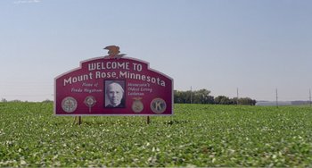 Movie still from “Drop Dead Gorgeous” (1999), directed by Michael Patrick Jann – A red sign in a field of green grass with an eagle on top of it; Extreme Wide shot, High angle