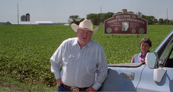 Movie still from “Drop Dead Gorgeous” (1999), directed by Michael Patrick Jann – An older man wearing a cowboy hat standing next to a blue truck; Medium shot, High angle